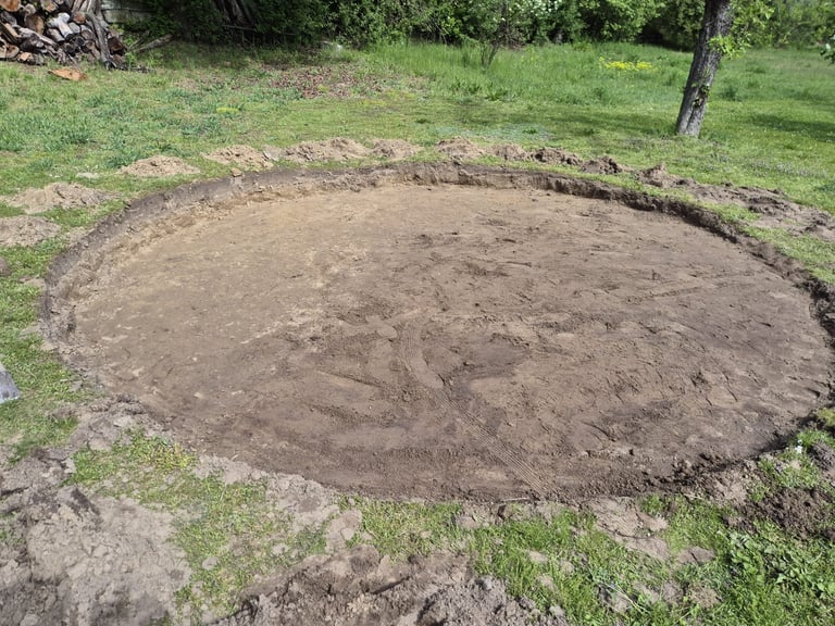 Large oval dirt excavation in grassy area with surrounding green lawn and scattered logs