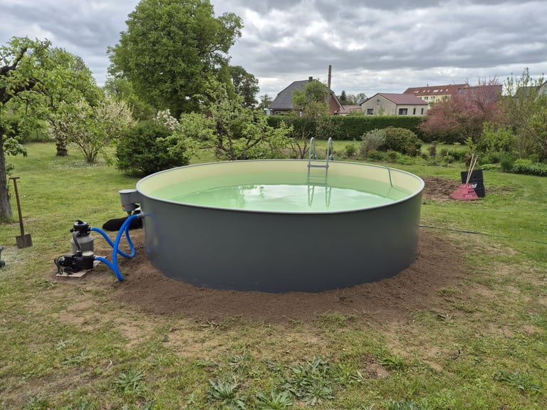 Large circular green pool under construction in a residential backyard with trees and houses in the background