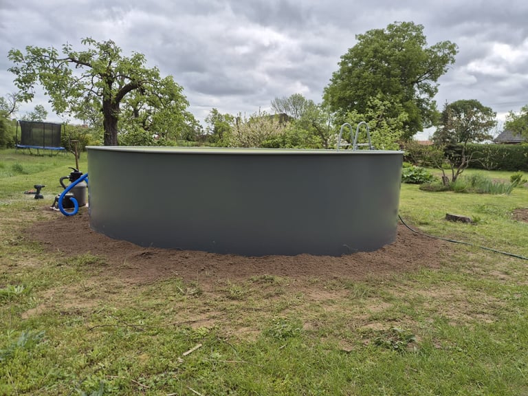 Large dark circular water tank installed in a grassy rural field with trees in the background and a person standing nearby